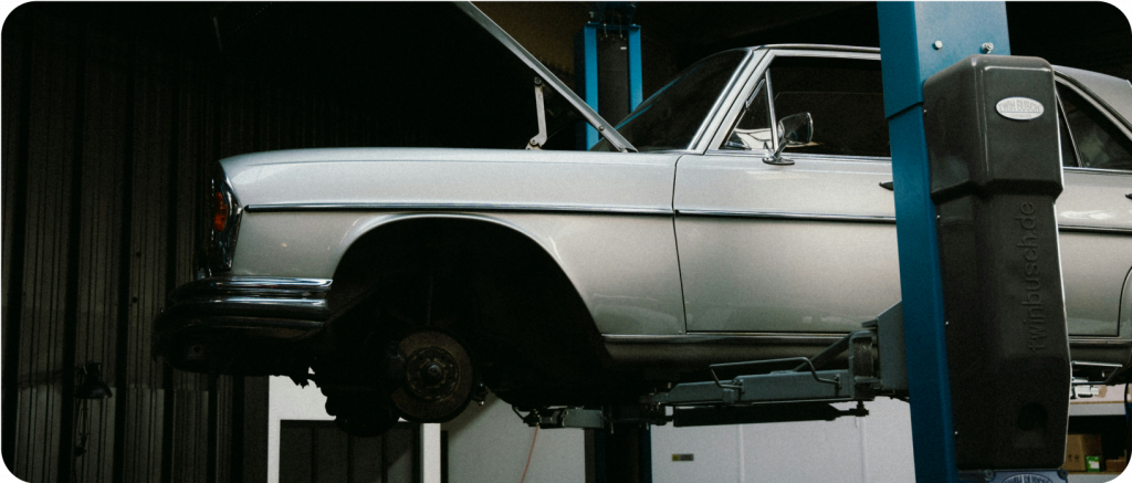 Véhicule sur pont élévateur dans un atelier, capot ouvert pour inspection mécanique.
