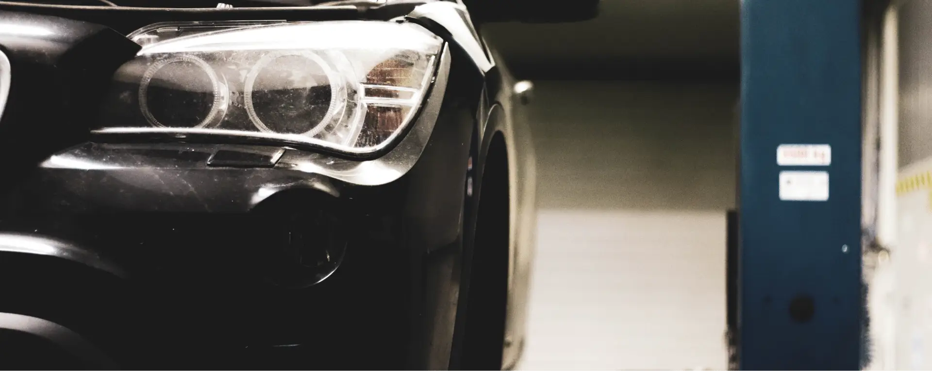 Vue rapprochée de l’avant d’un véhicule dans un garage, avec le projecteur allumé et l’auto positionnée près d’un pont élévateur.